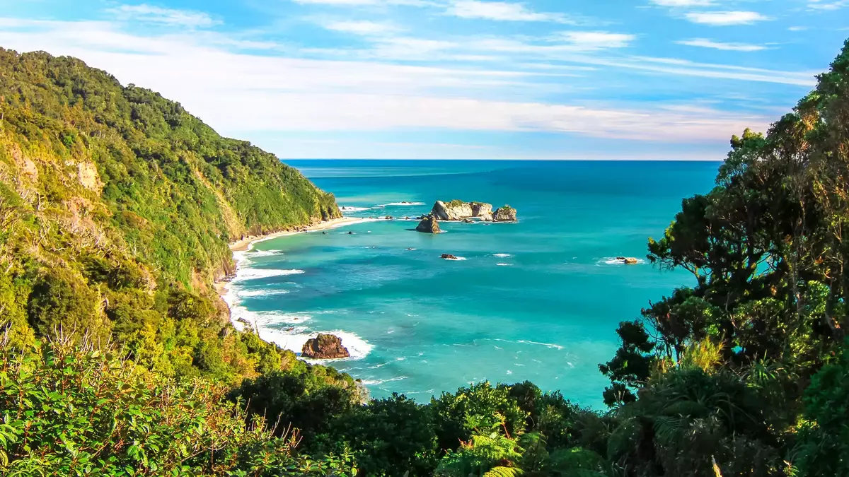 Blue sky background with a Rainforest mountain in the foreground that meets the turquoise blue sea.  Main Image