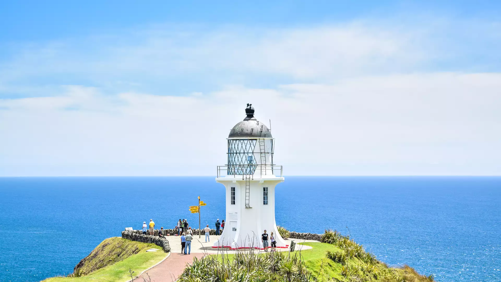 White lighthouse on cliff edge with people and vast blue ocean under a partly cloudy sky Credit: Fine Tours Group - Photographer unknown Main Image