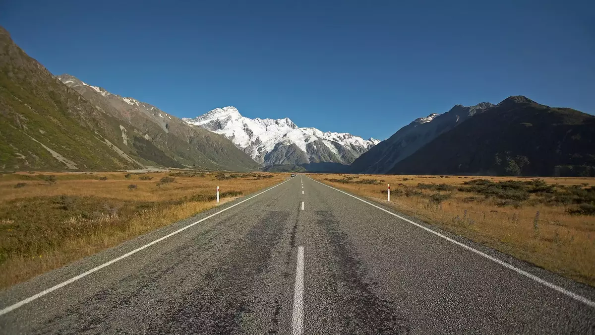 Road stretching towards snow-capped Aoraki Mount Cook with mountains and clear blue sky Main Image
