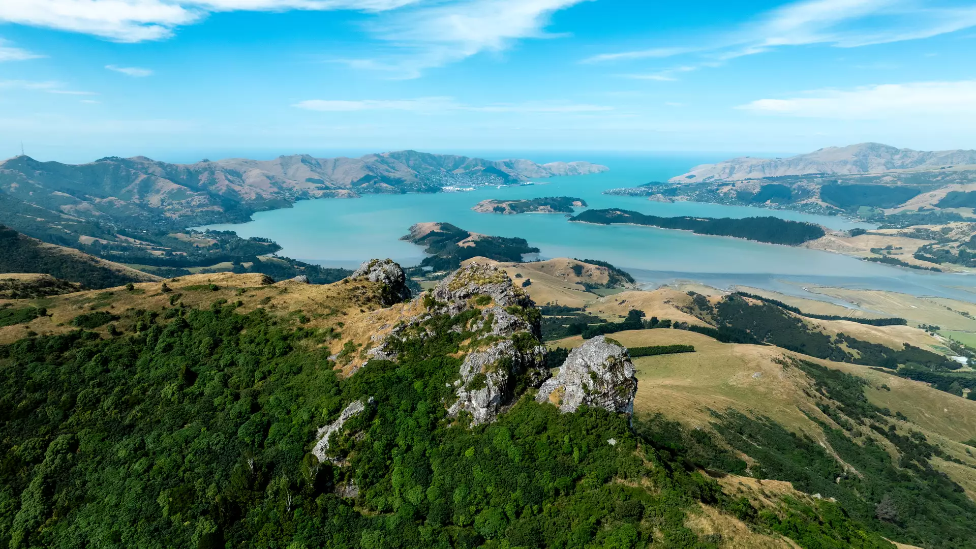 Aerial view of jagged rock outcrops on the Port Hills overlooking the turquoise Lyttelton Harbour. Credit: Christchurch NZ Main Image