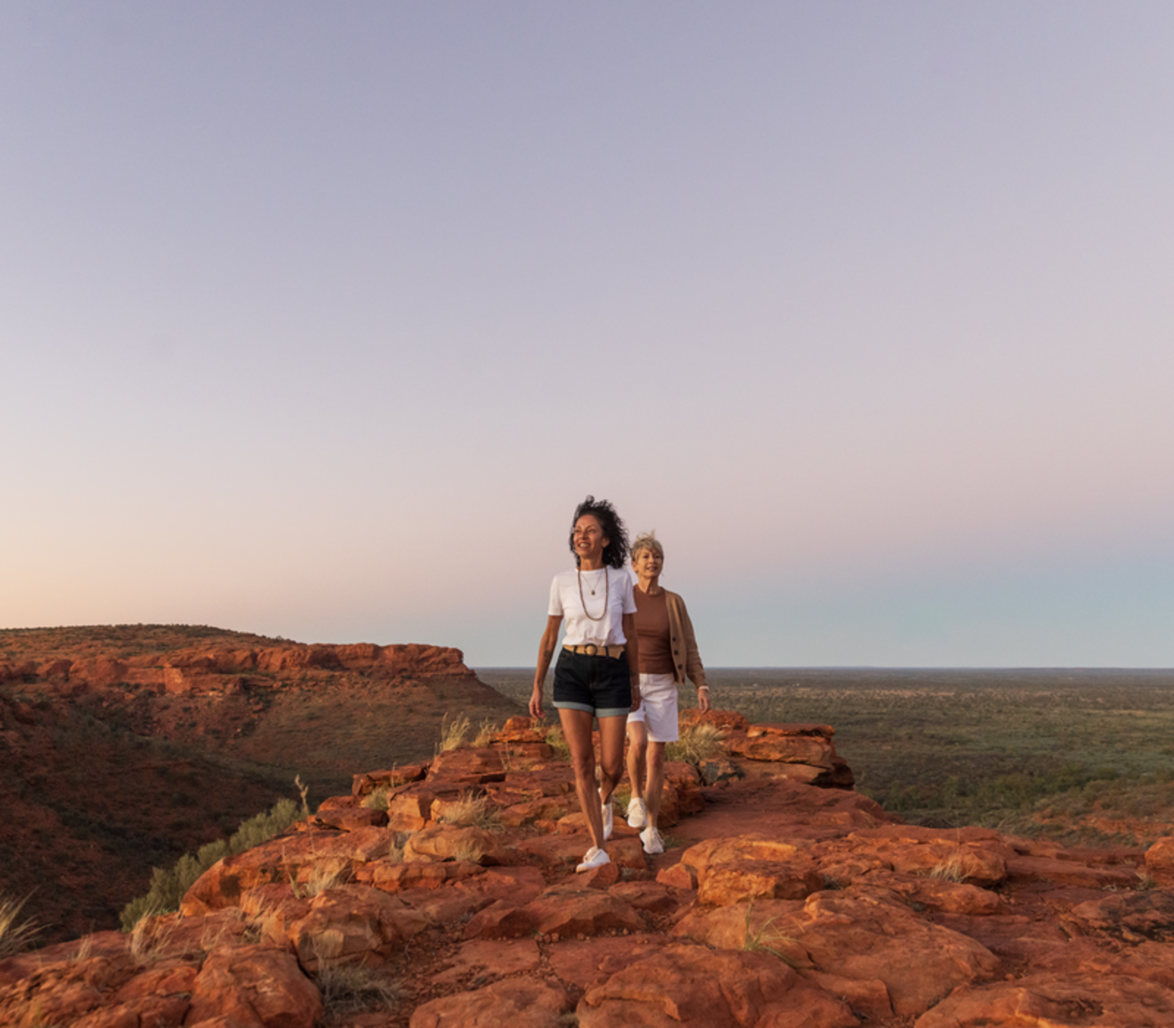 Two women walking along a red rock ridge at Kings Canyon in the Northern Territory during golden hour.