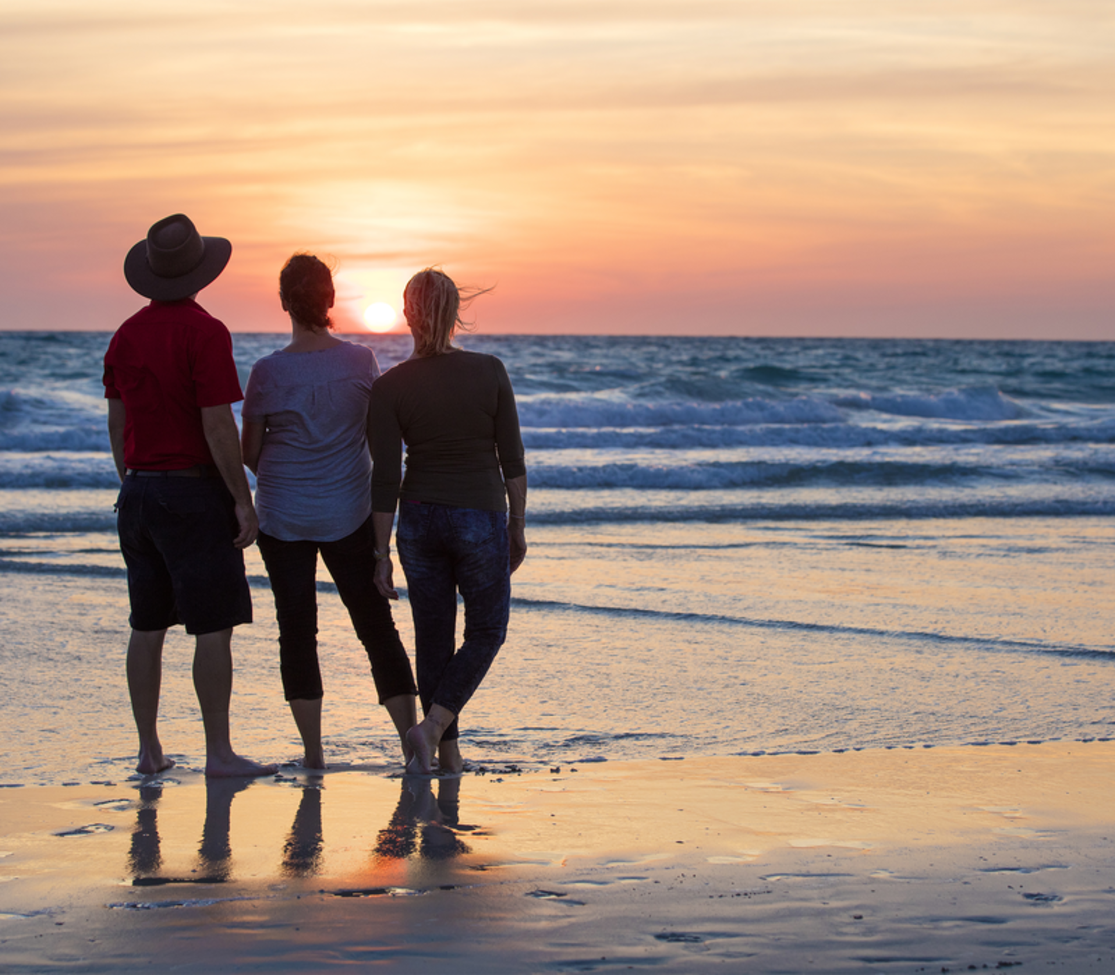 Three people silhouetted against a golden sunset on Cable Beach in Broome, Western Australia.