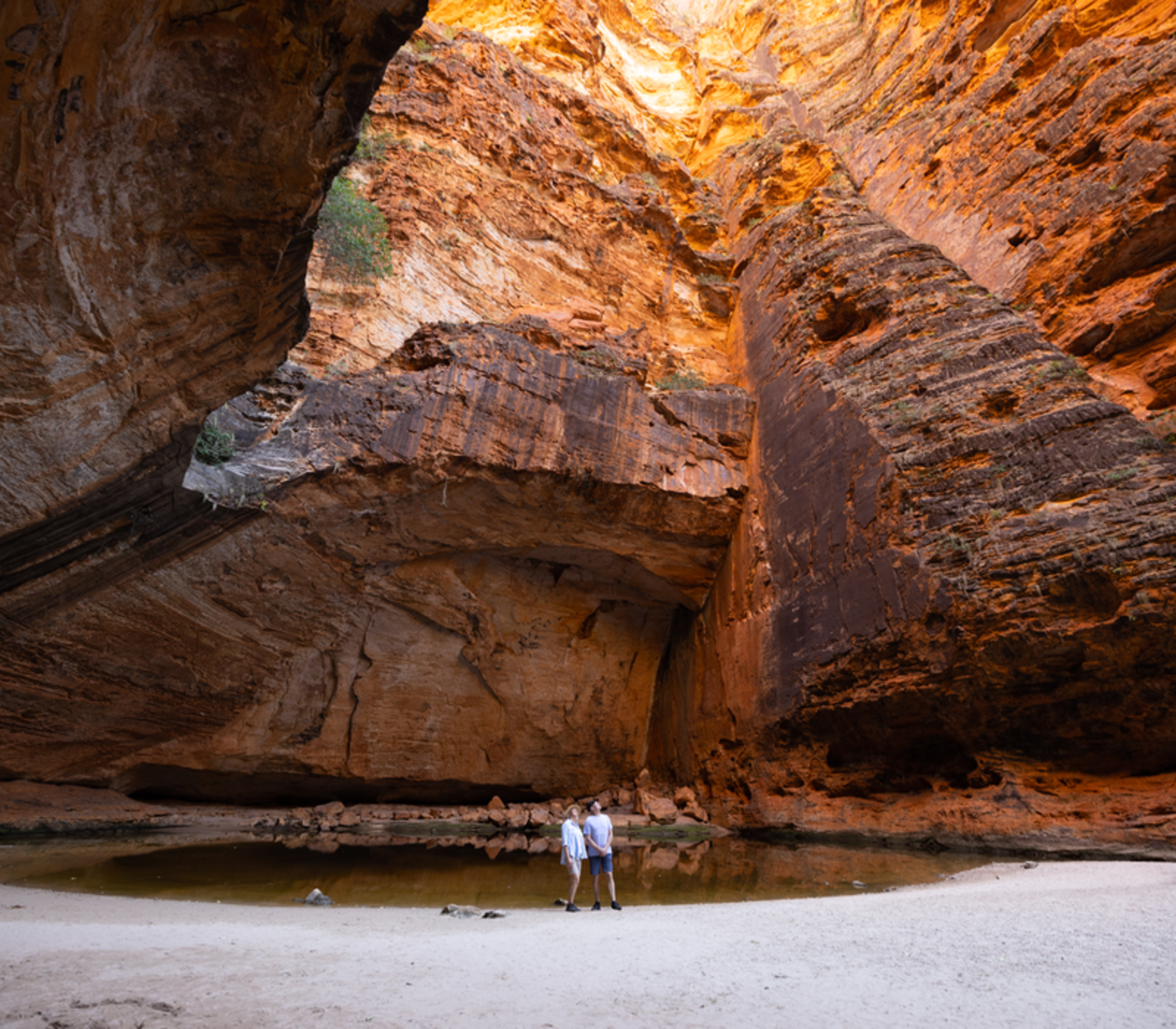 A wide interior shot of the orange rock walls of Cathedral Gorge reflecting in a dark pool of water.