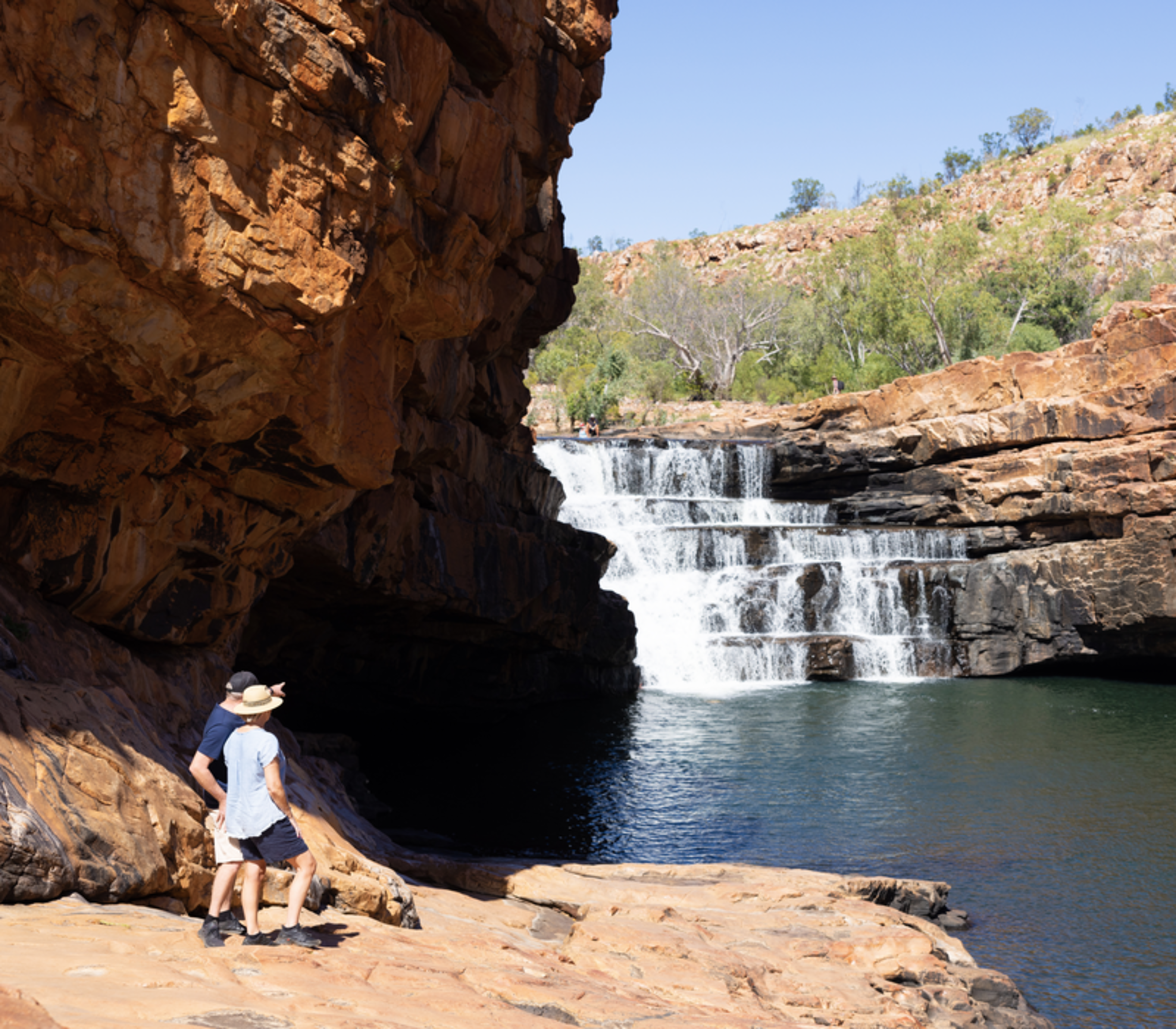A multi-level waterfall cascading into a dark green pool surrounded by steep orange rock walls in Western Australia.