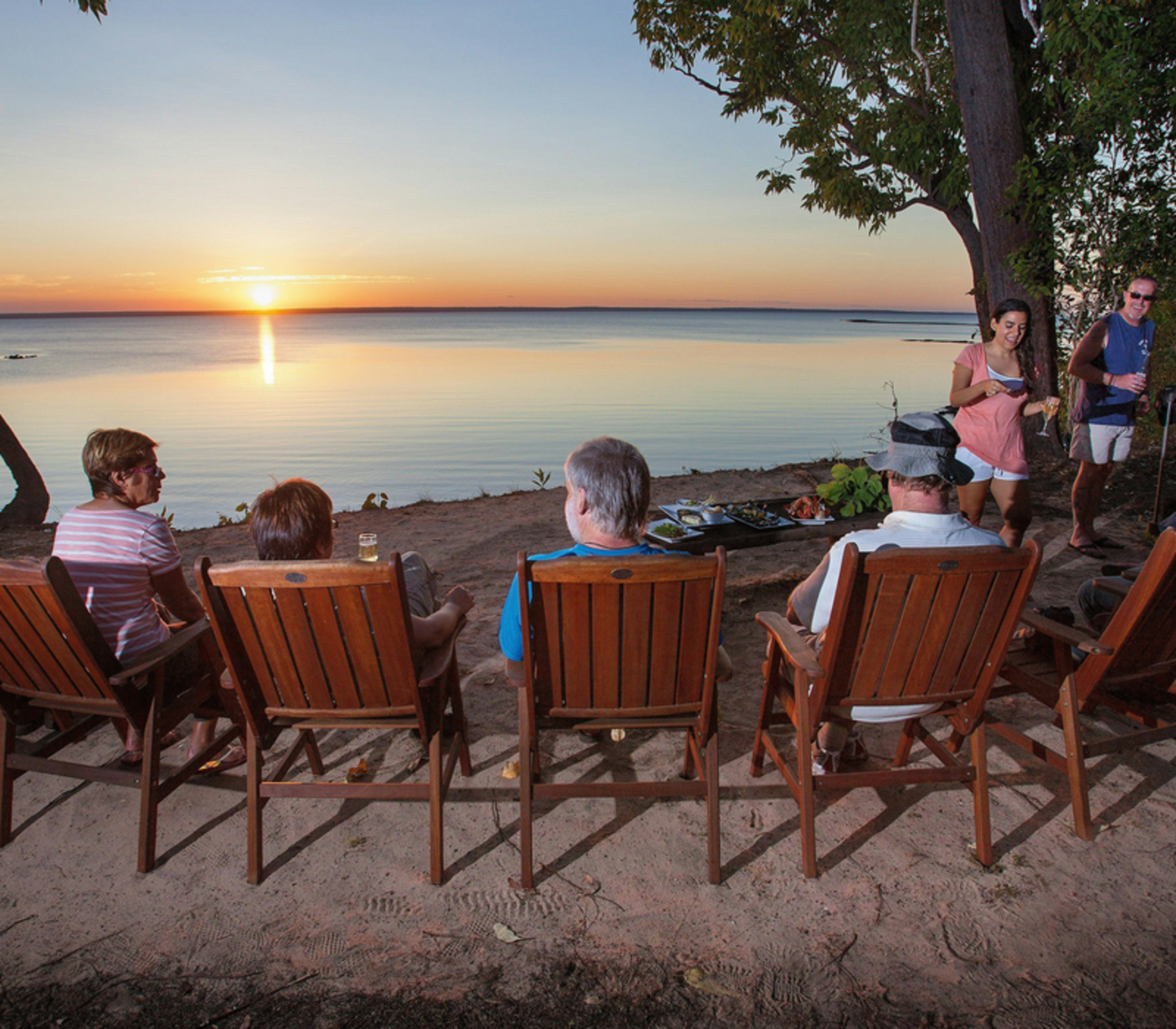 Travelers sitting in wooden chairs watching a sunset over water in the Top End.