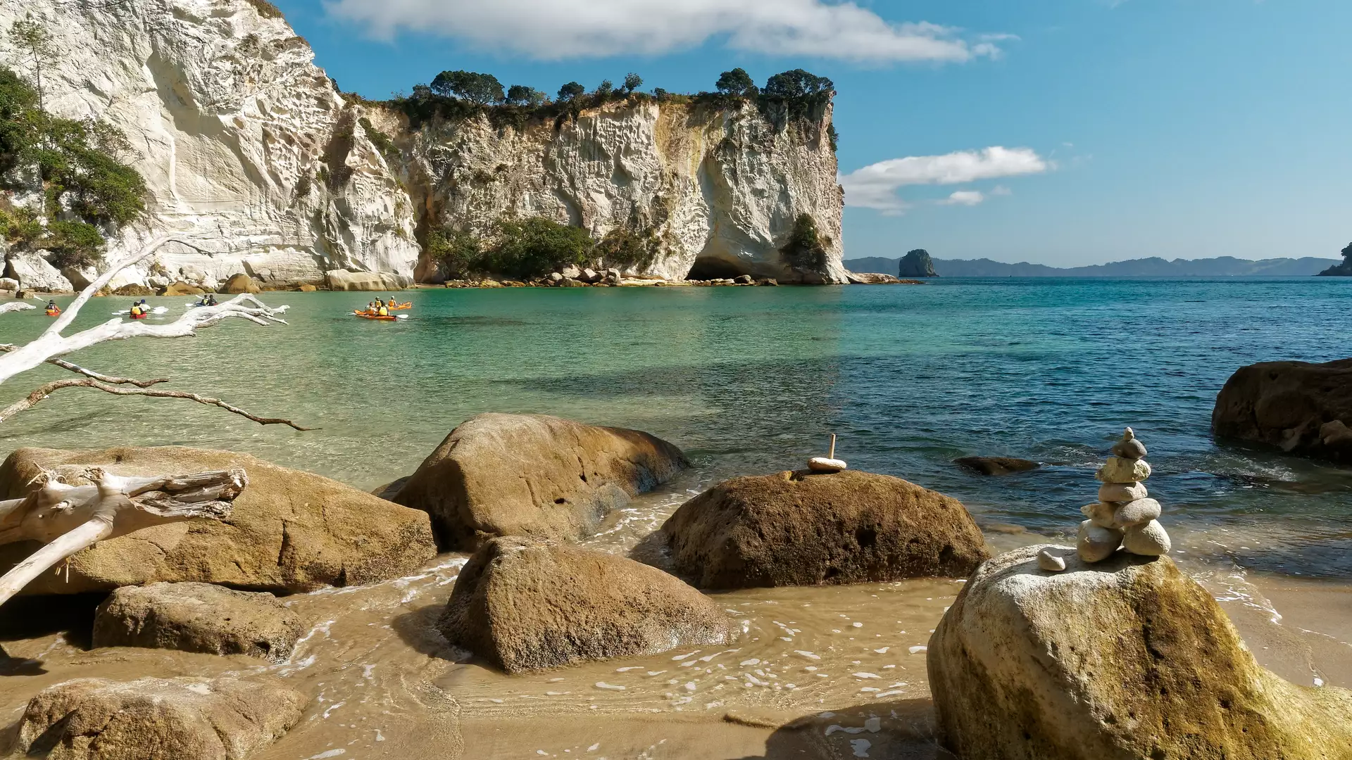 Rocky sandy beach with kayakers on turquoise water and white cliffs in the background under blue sky. Credit: Fine Tours Group - Photographer unknown Main Image