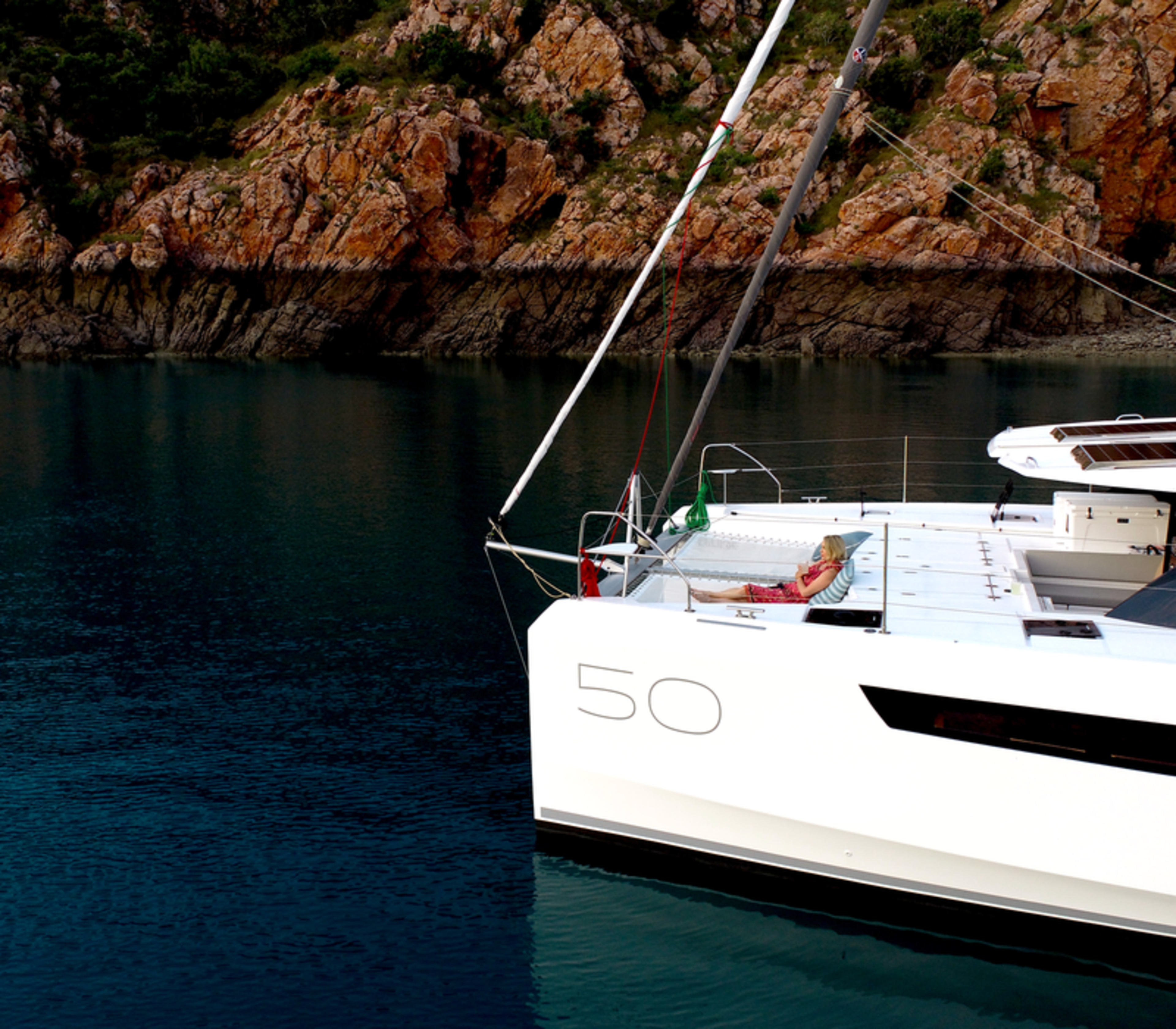 Woman relaxing on an Eclipse Expeditions luxury catamaran in front of red Kimberley cliffs at Dugong Bay.