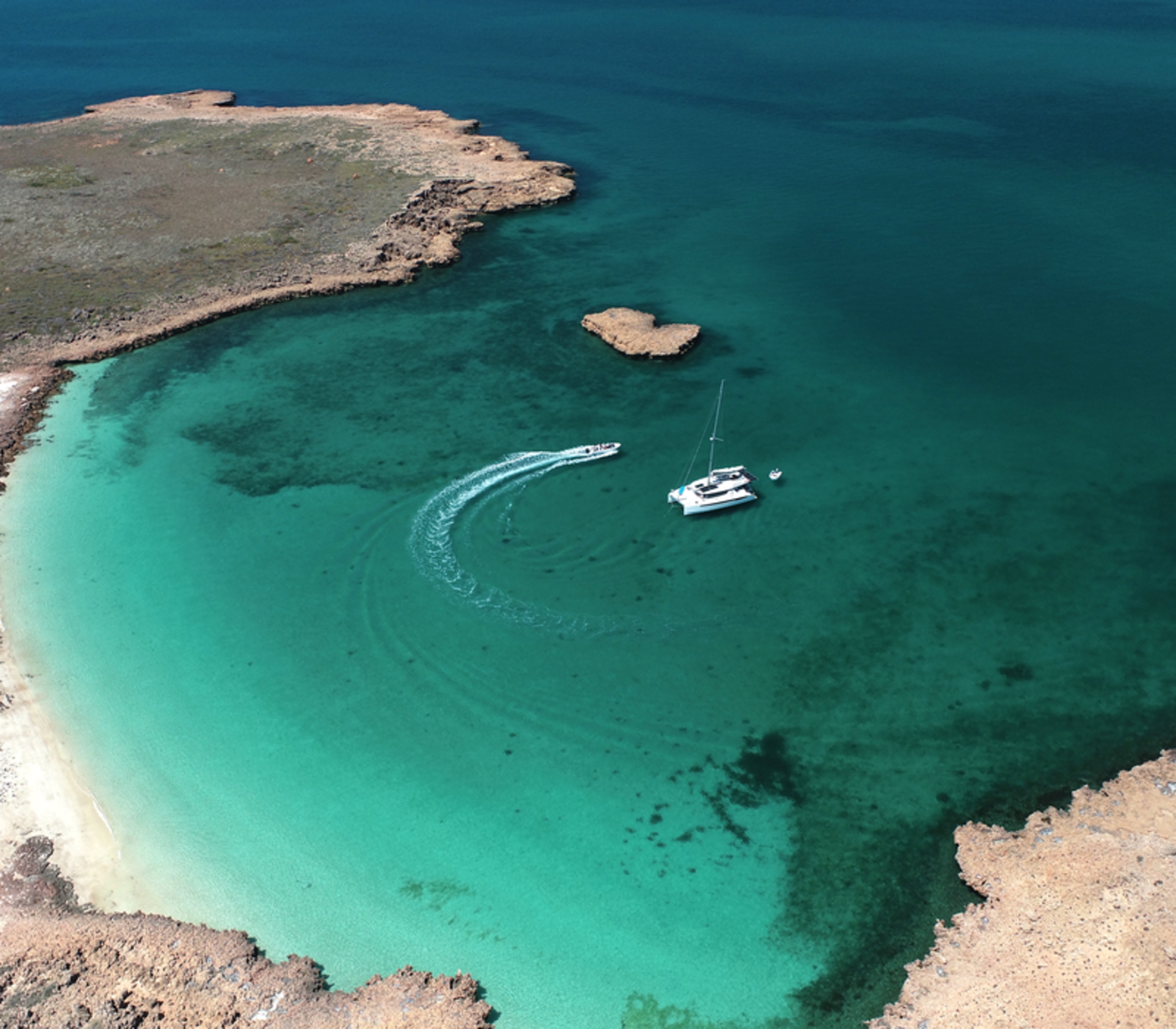High angle drone shot of a white catamaran in a clear turquoise bay at Delta Island, Western Australia.