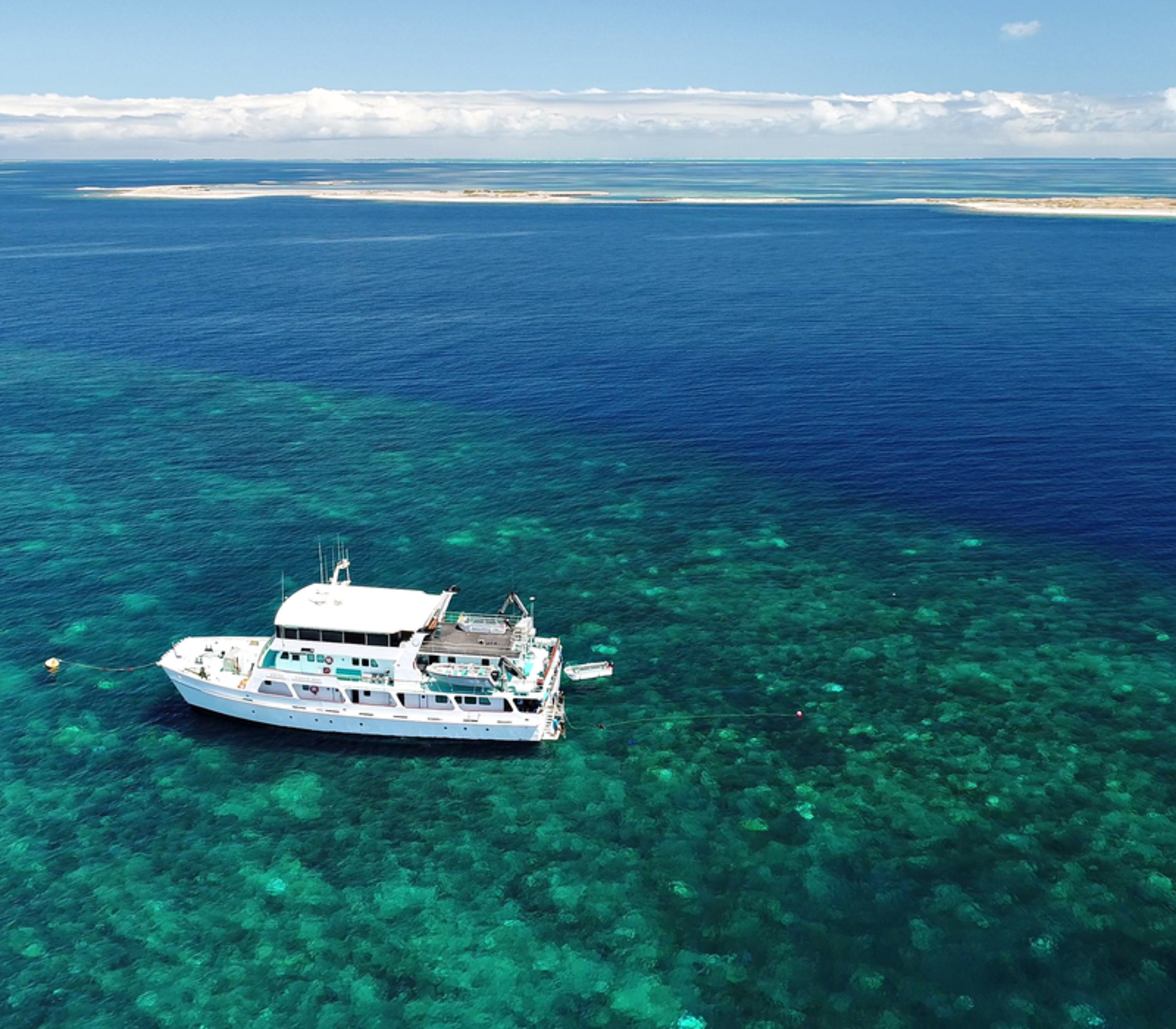 An aerial view of an Eco Abrolhos Cruise vessel anchored in the vibrant, turquoise coral reefs of Western Australia.