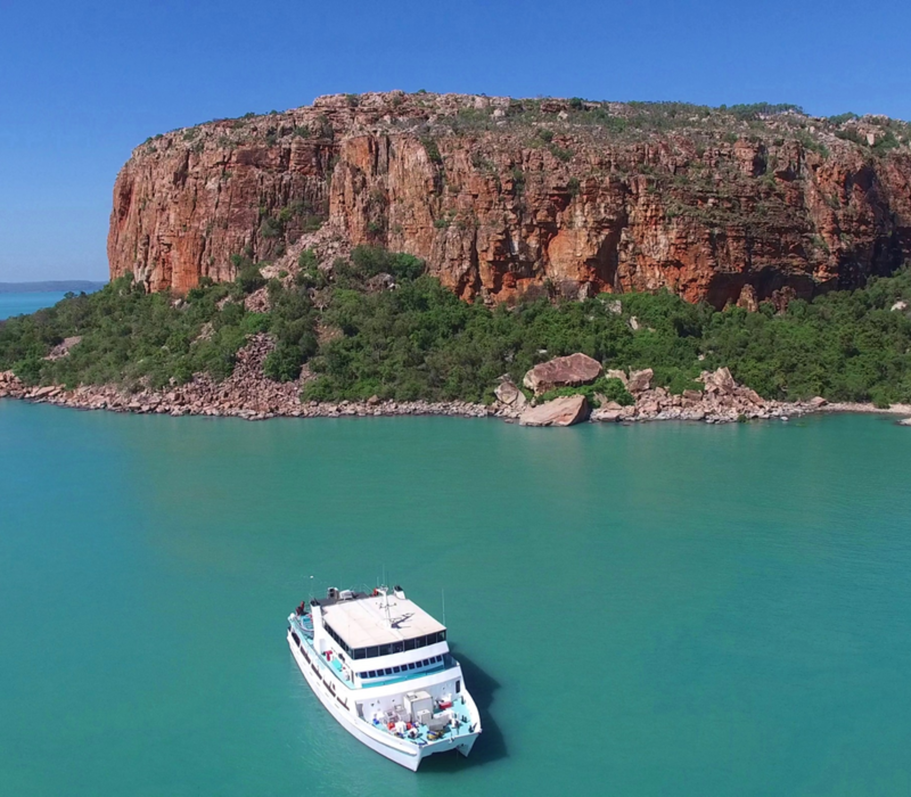 An Eco Abrolhos Cruise vessel sits in the turquoise waters beside a dramatic flat-topped island in Western Australia.