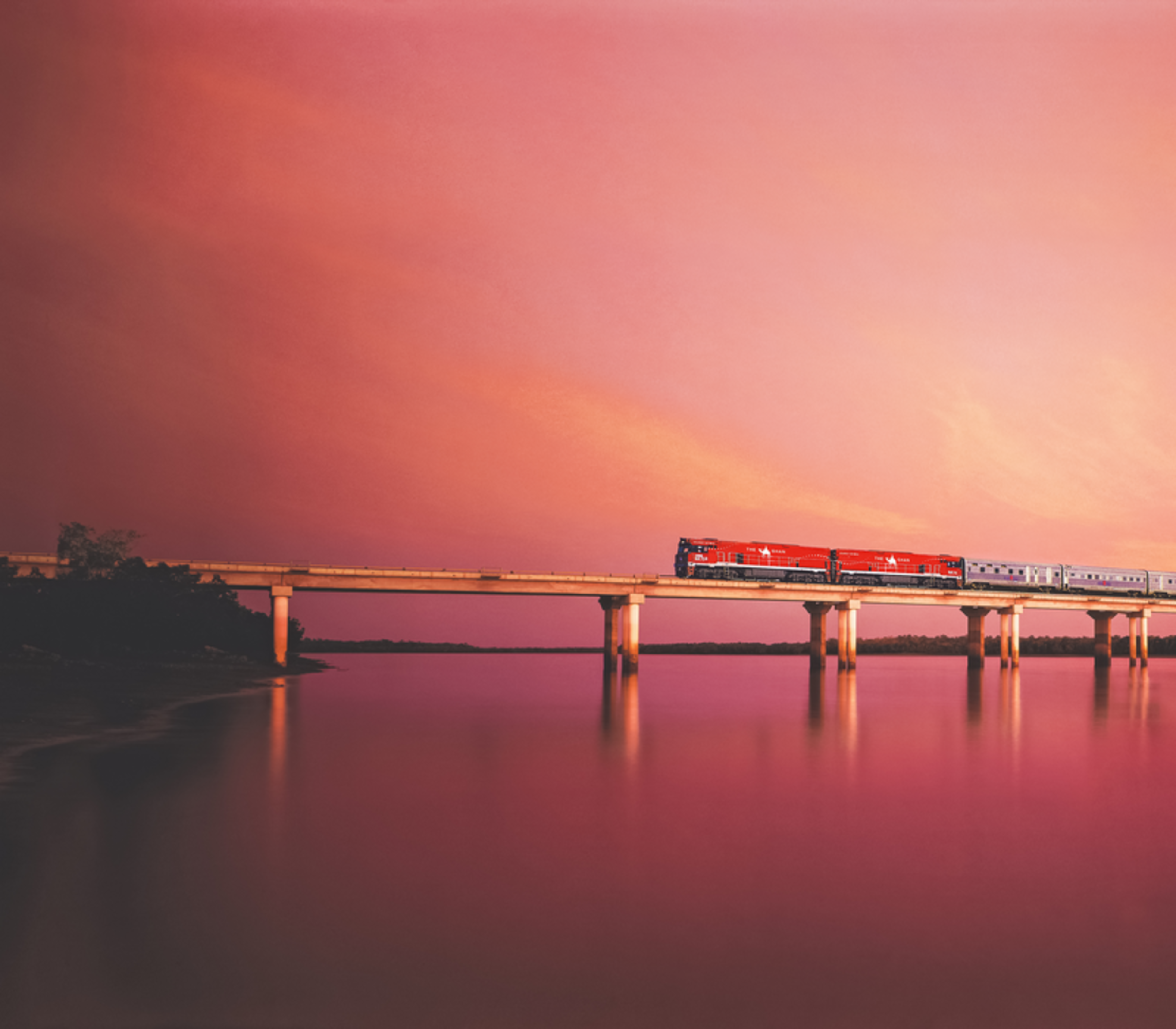 Dramatic image of The Ghan crossing a bridge over the Elizabeth River at sunset.