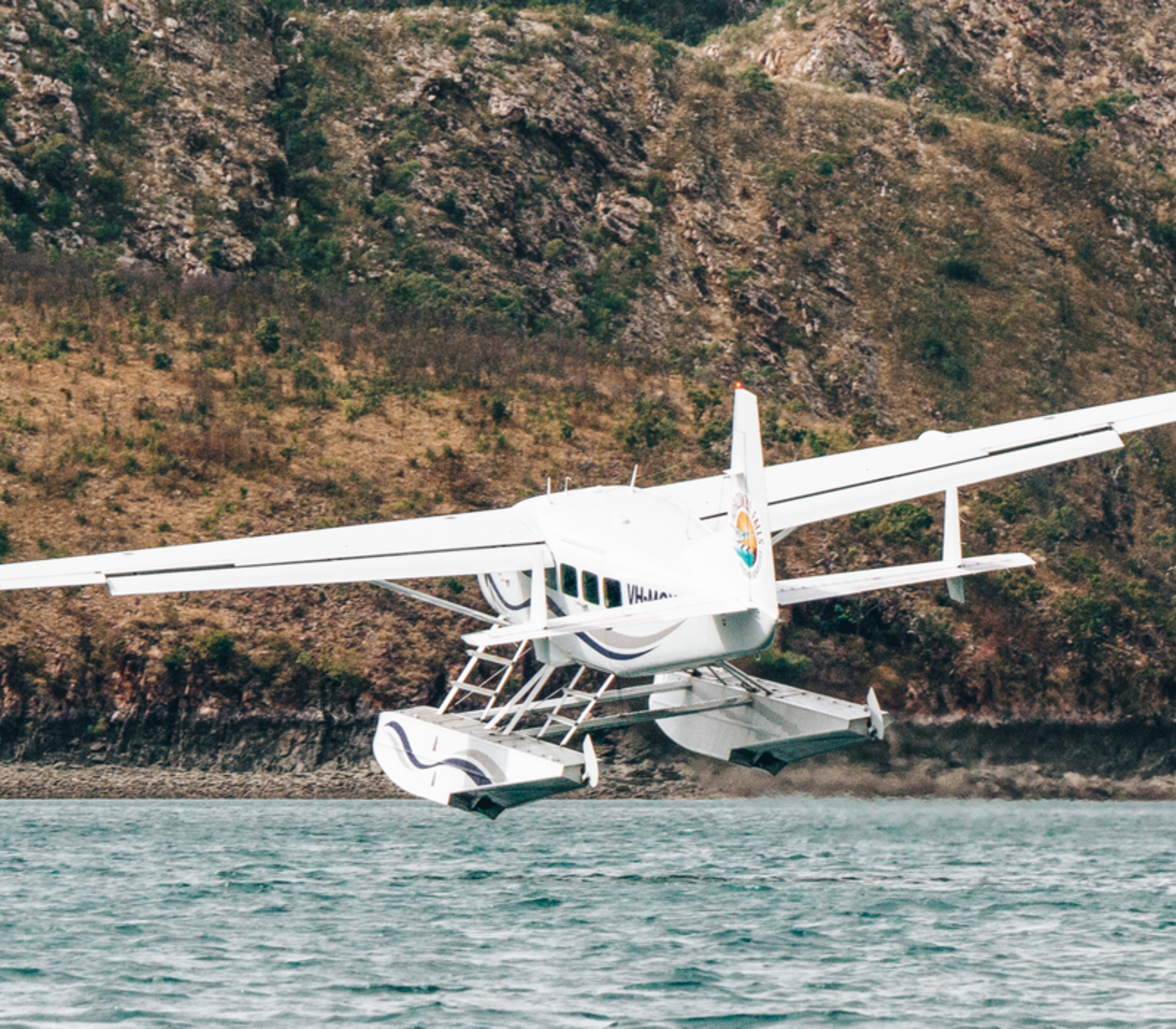 White seaplane in mid-takeoff from the ocean against a backdrop of rugged Kimberley mountains.