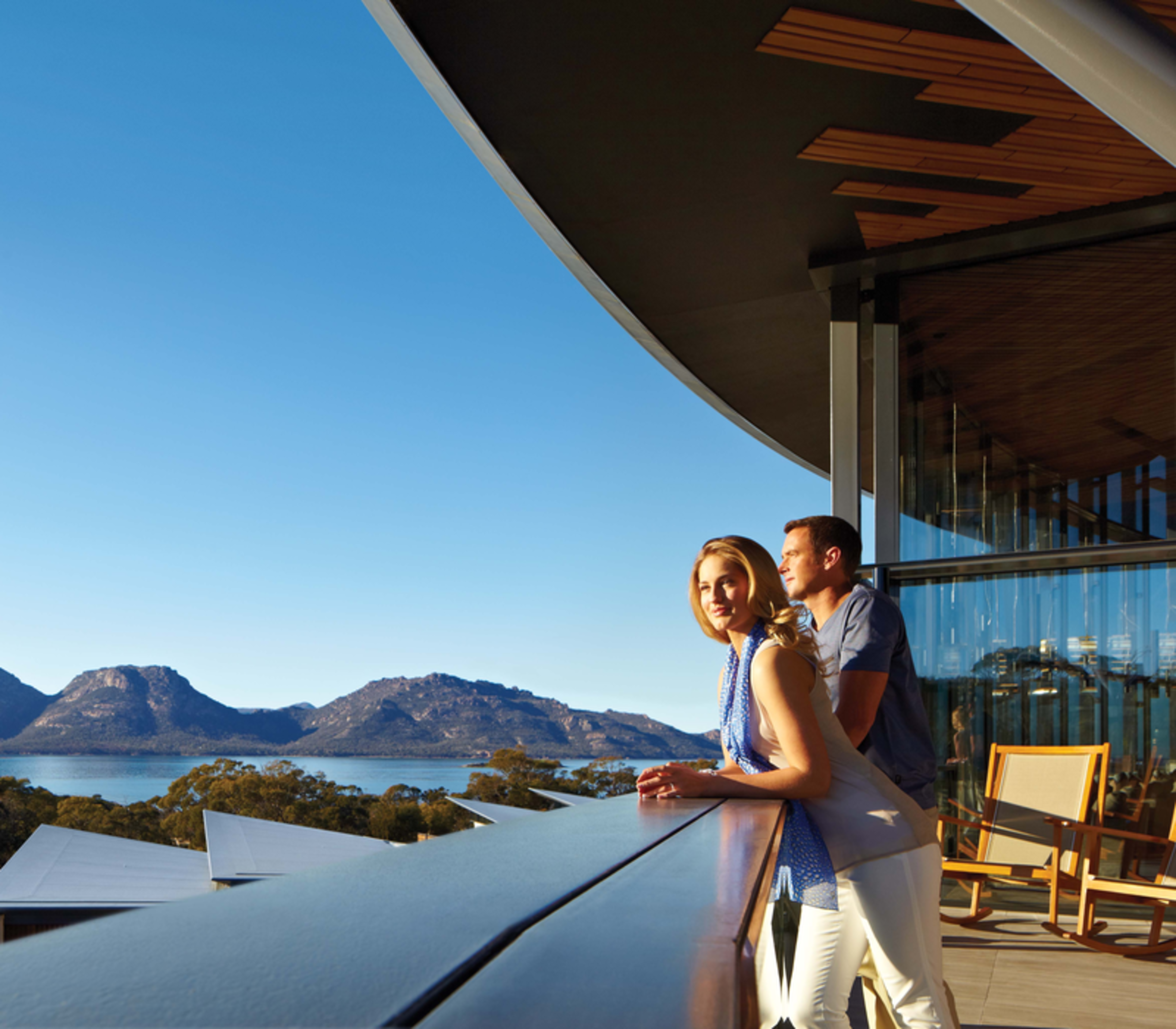 Guests relaxing on the expansive outdoor timber deck of Saffire Freycinet, offering a premier vantage point over the Great Oyster Bay and the Hazards mountain range.
