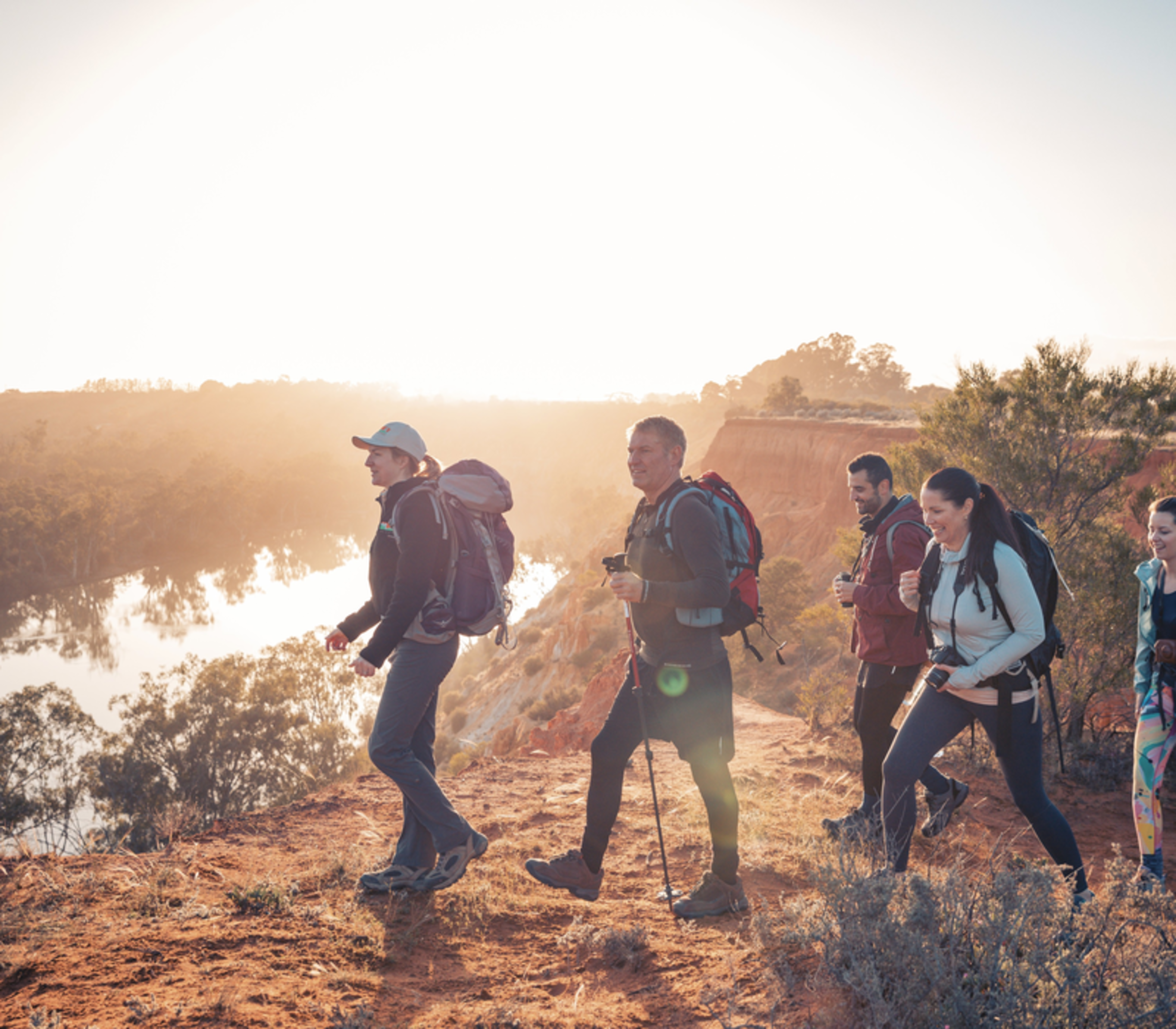 Silhouetted hikers walking along a cliff edge at sunset overlooking the Murray River.