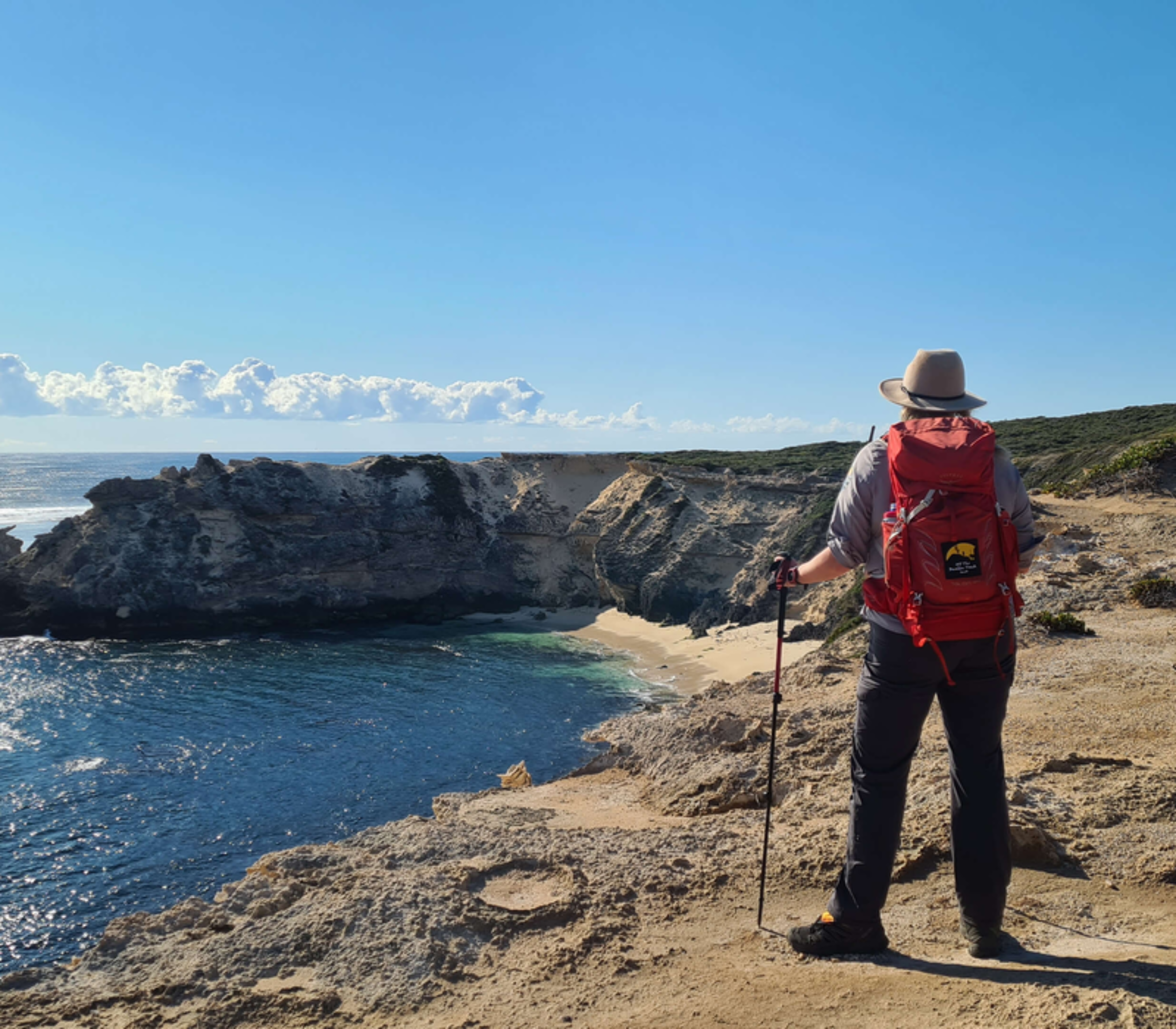 Hiker with a red pack looking down at the pristine white sands and blue water of Horseshoe Bay.