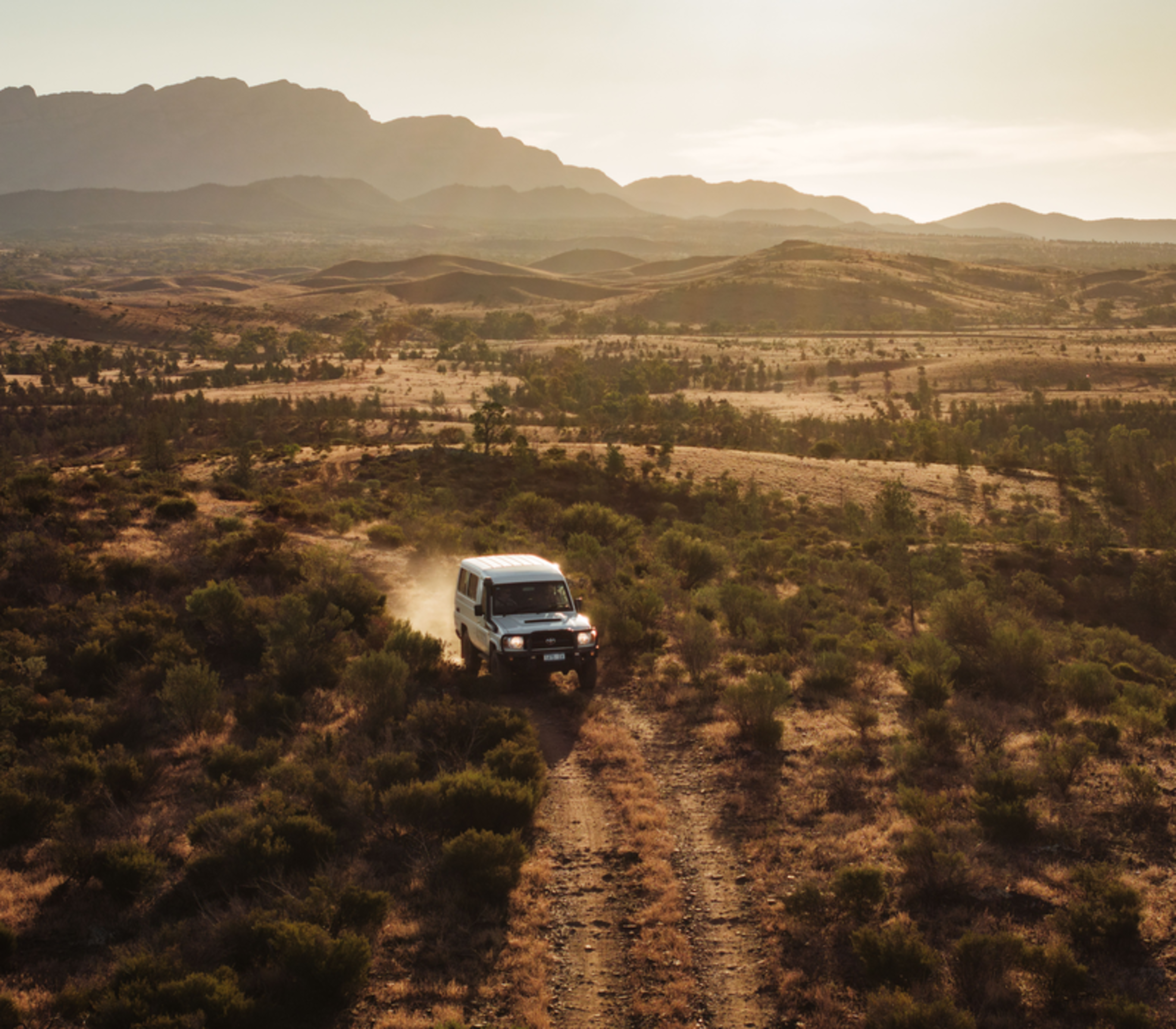 A 4WD vehicle driving through the golden-lit outback terrain of Rawnsley Park Station in South Australia.