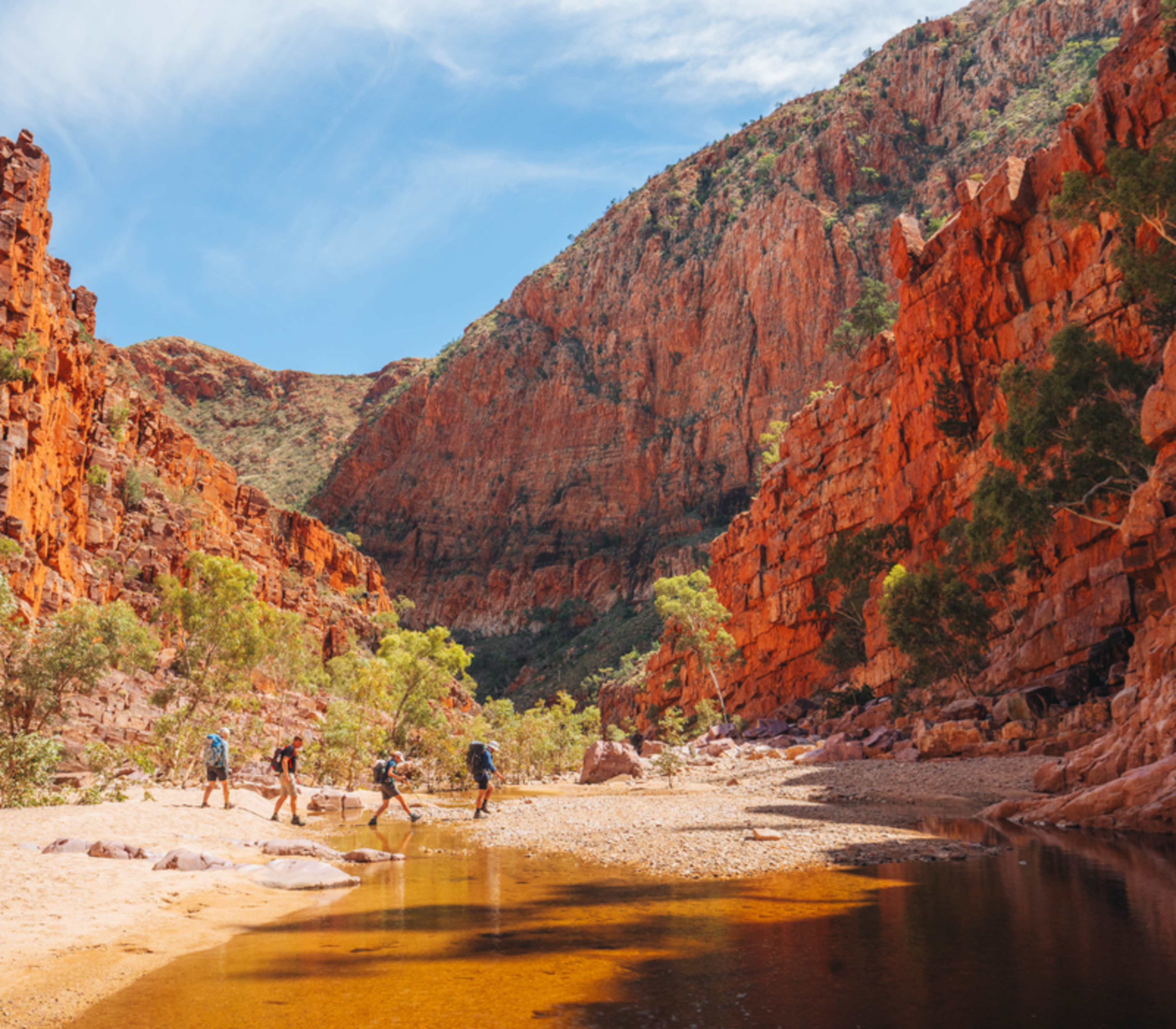 Guided hiking group walking through the massive red rock walls of Ormiston Gorge in the Northern Territory.