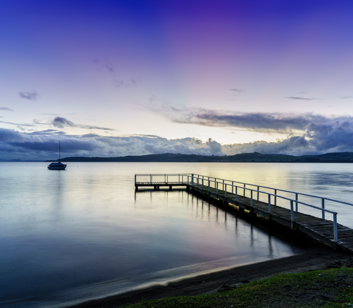 Wooden pier extending into calm lake water with a boat and sunset sky in the background Main Image
