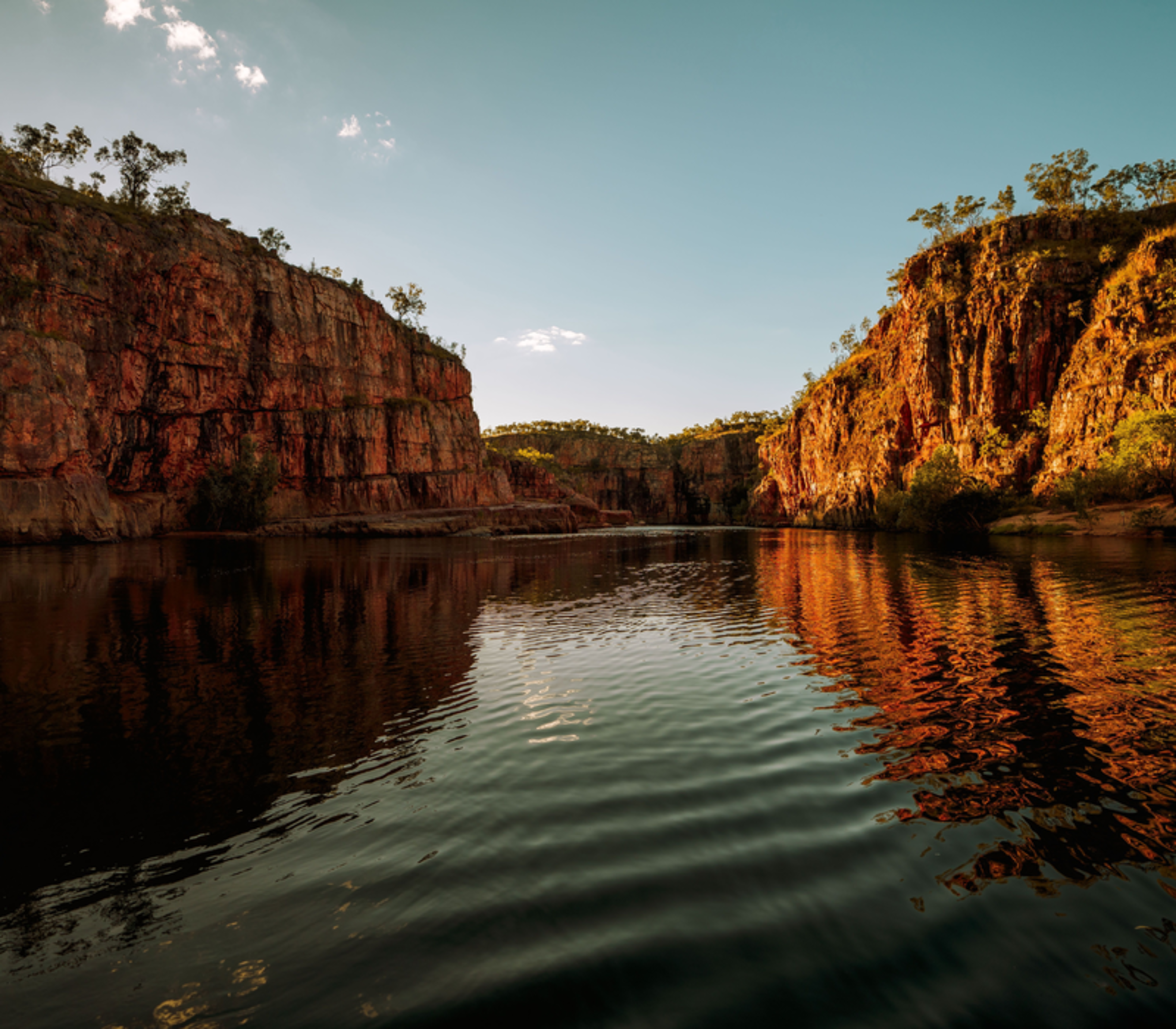 A low-angle water perspective of the first gorge at Nitmiluk National Park, captured as the rising sun casts a golden glow on the vertical sandstone faces.