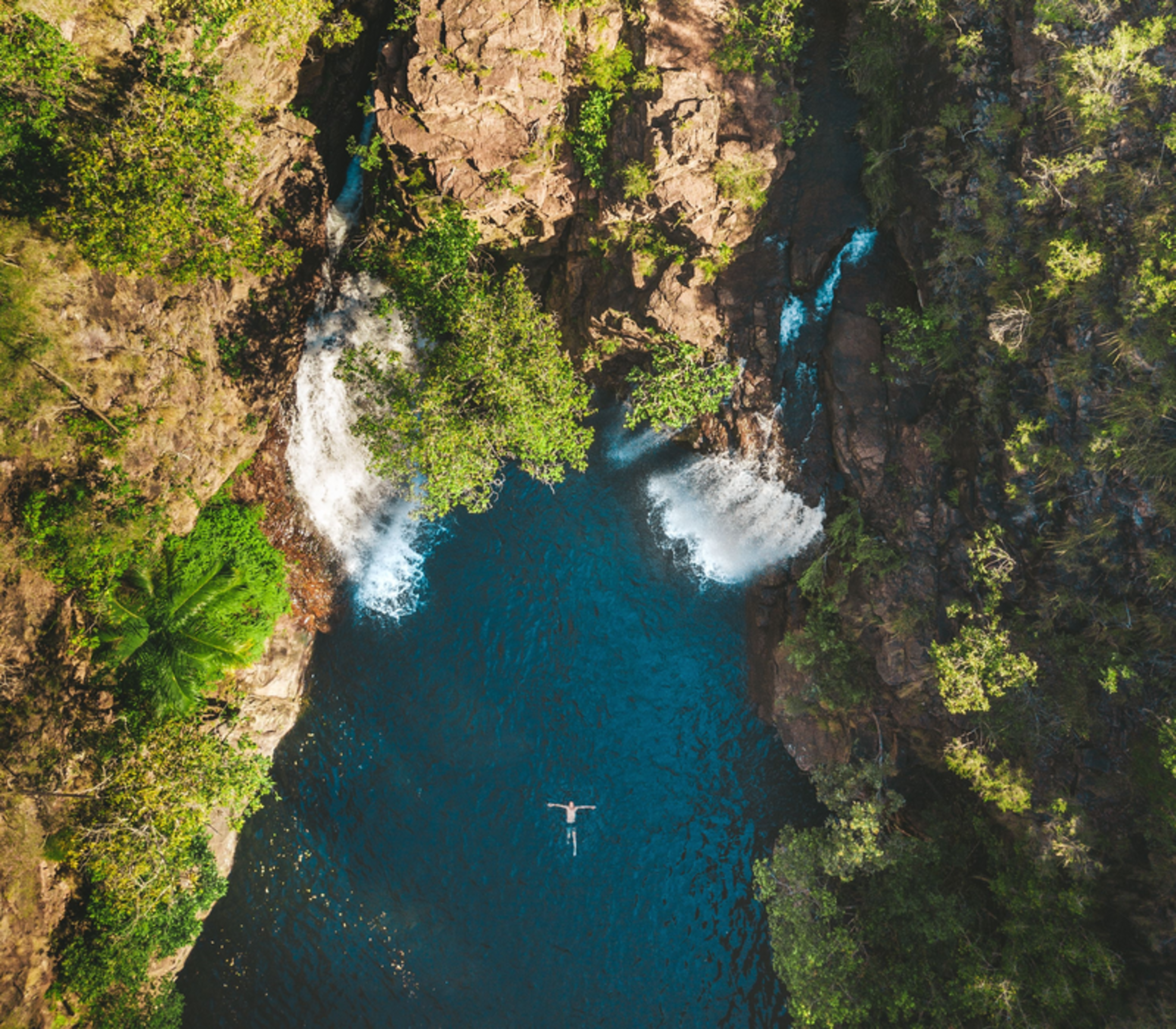 A high-angle vertical aerial shot looking directly down into the Florence Falls plunge pool and the lush monsoon forest surrounding the twin cascades.