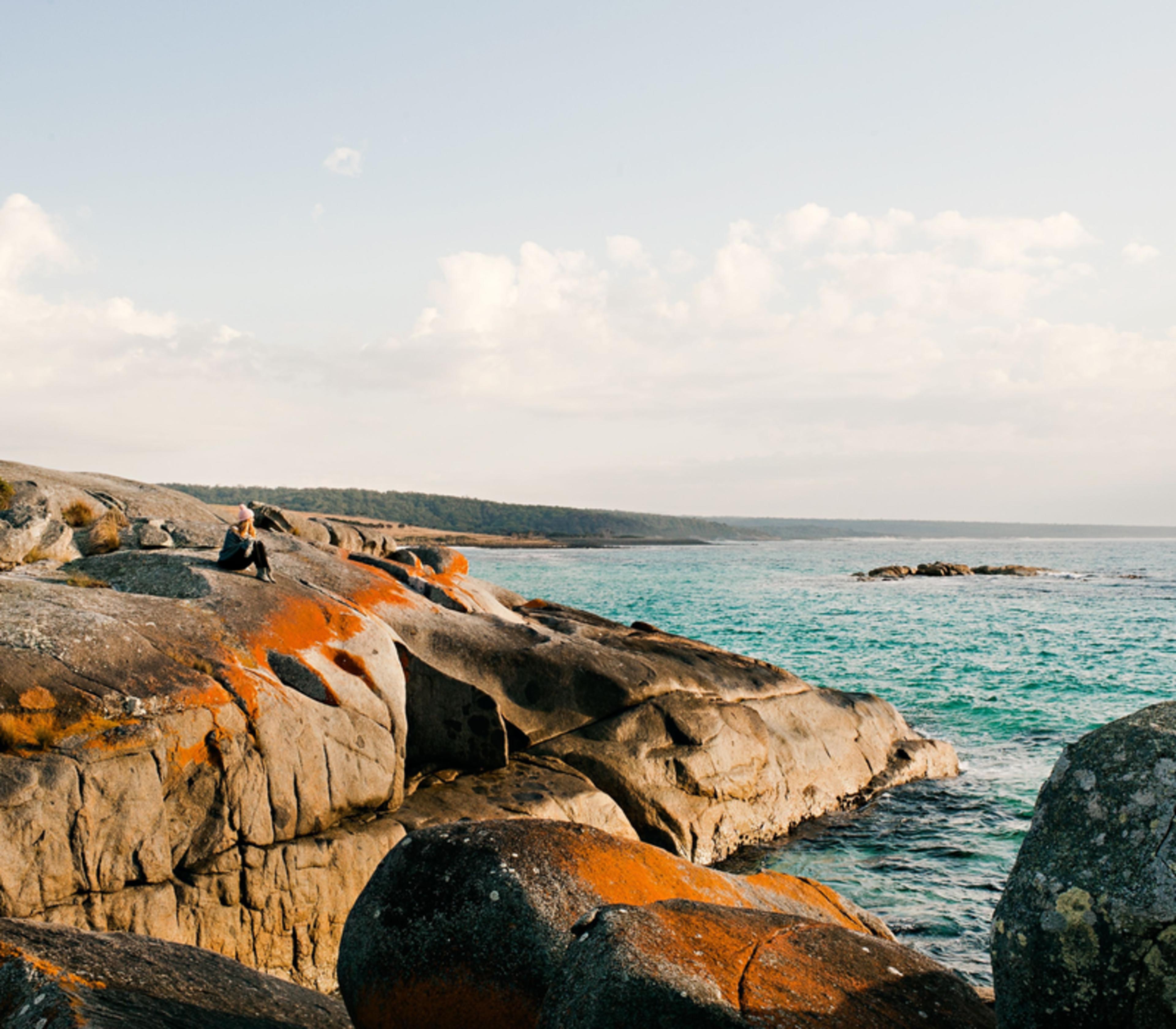 direct top-down aerial photograph of a secluded cove in the Bay of Fires, featuring crystal-clear turquoise water, white sand beach with footprints, and large granite boulders splashed with vibrant orange lichen.