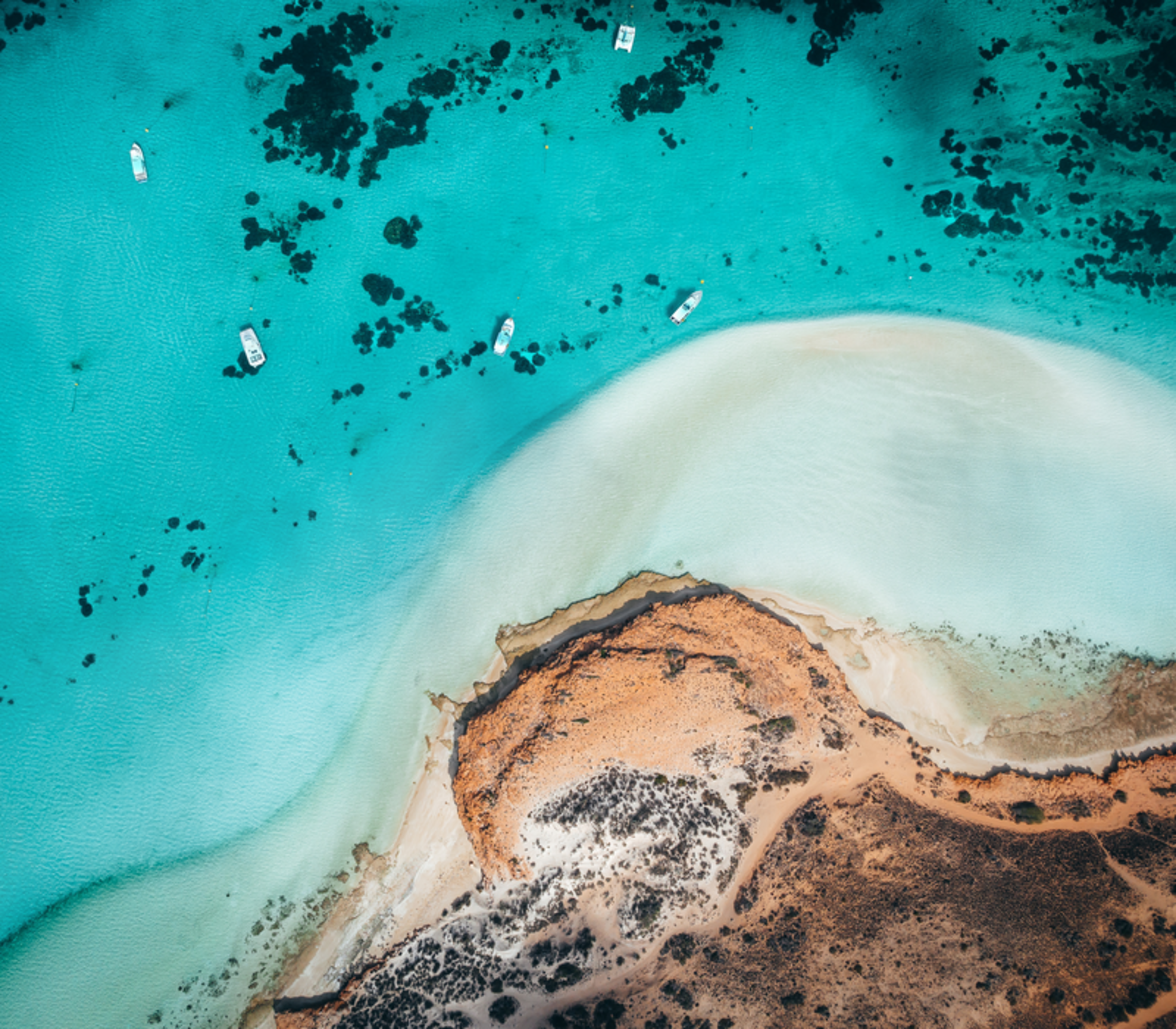 Aerial view of turquoise ocean channels winding through white sand banks and red earth in Shark Bay.