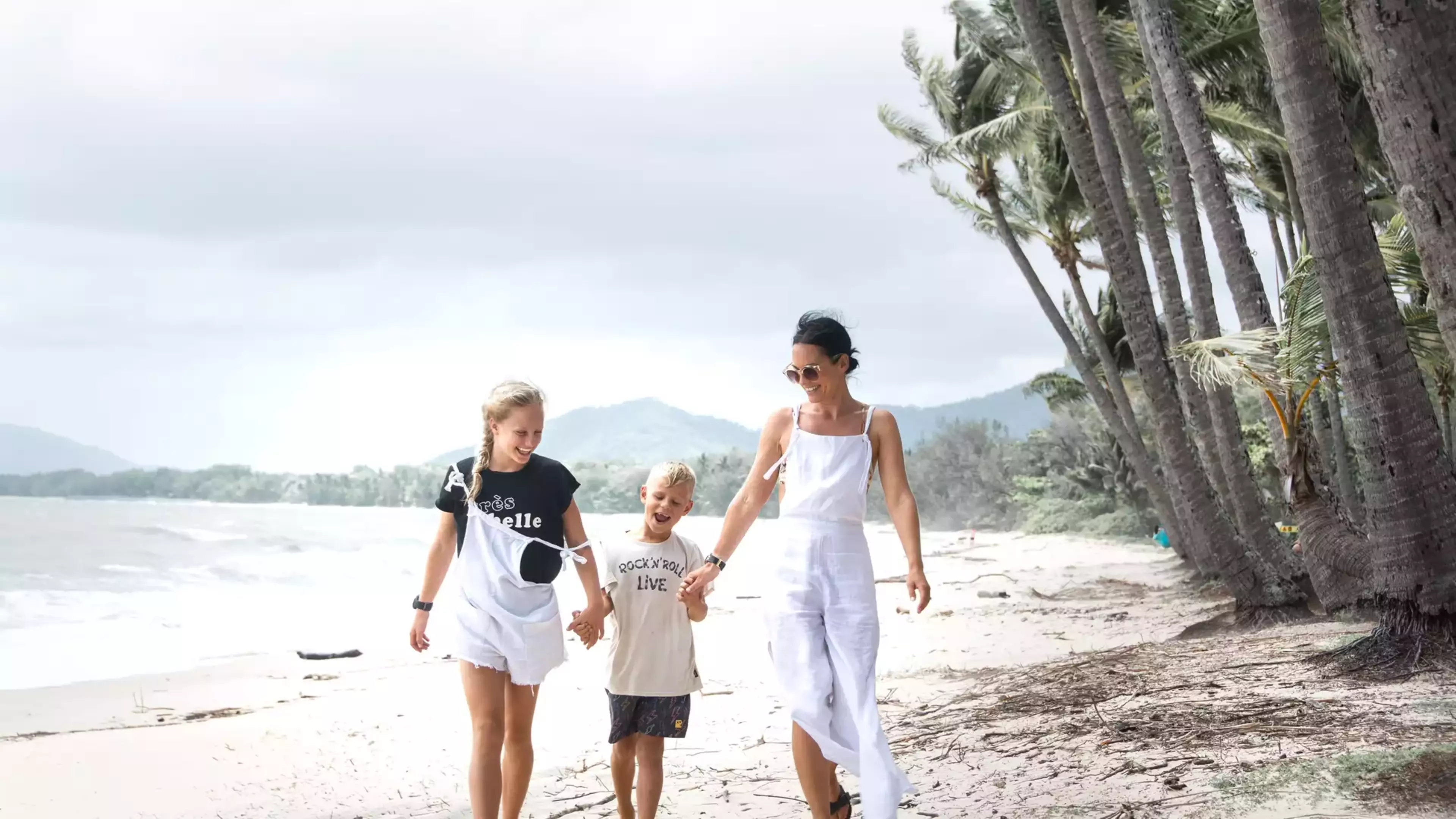 A happy family walking along the beach in Palm Cove under tropical palm trees in North Queensland.