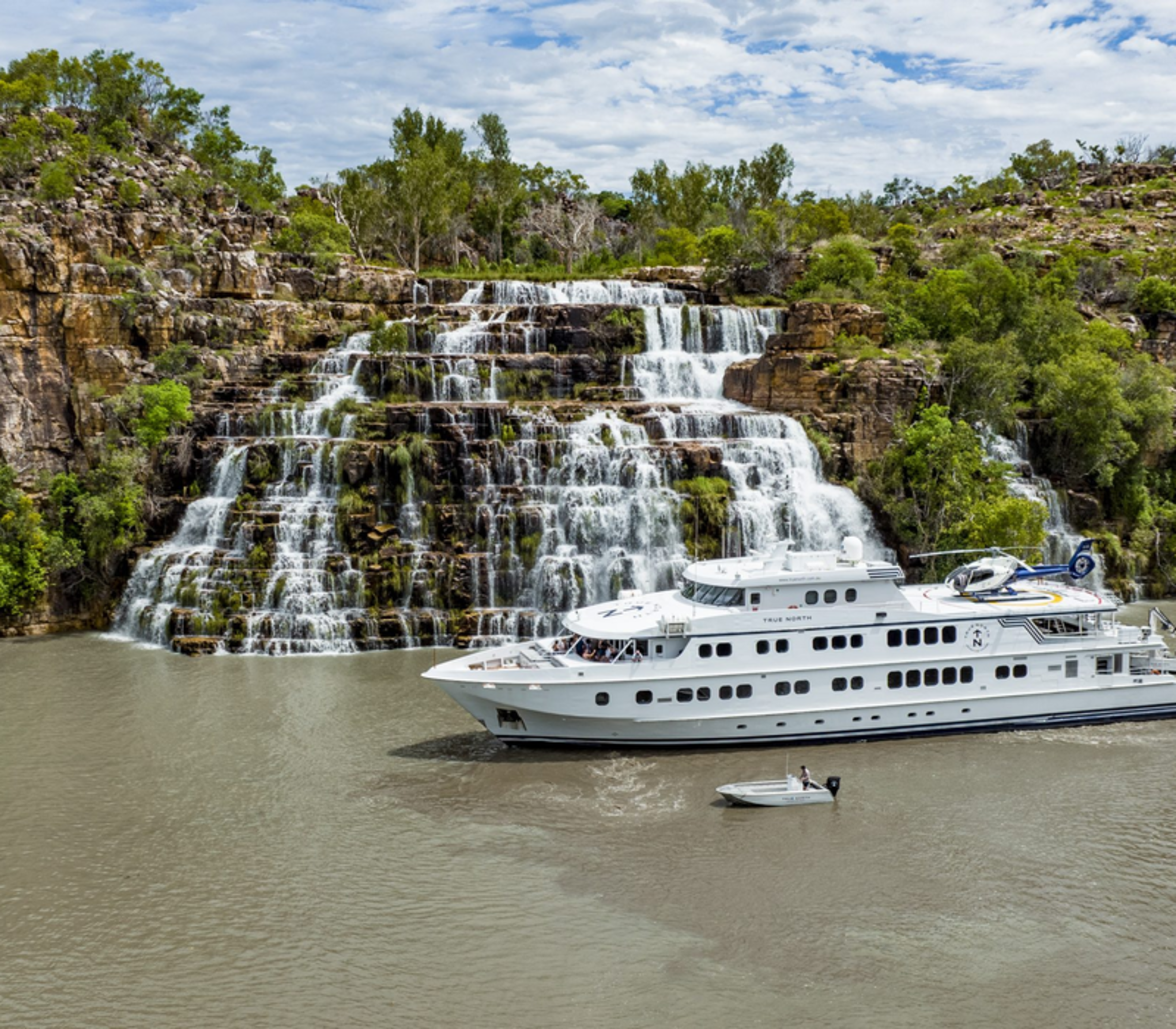 A luxury True North cruise ship positioned in front of a massive tiered sandstone waterfall in the Kimberley.
