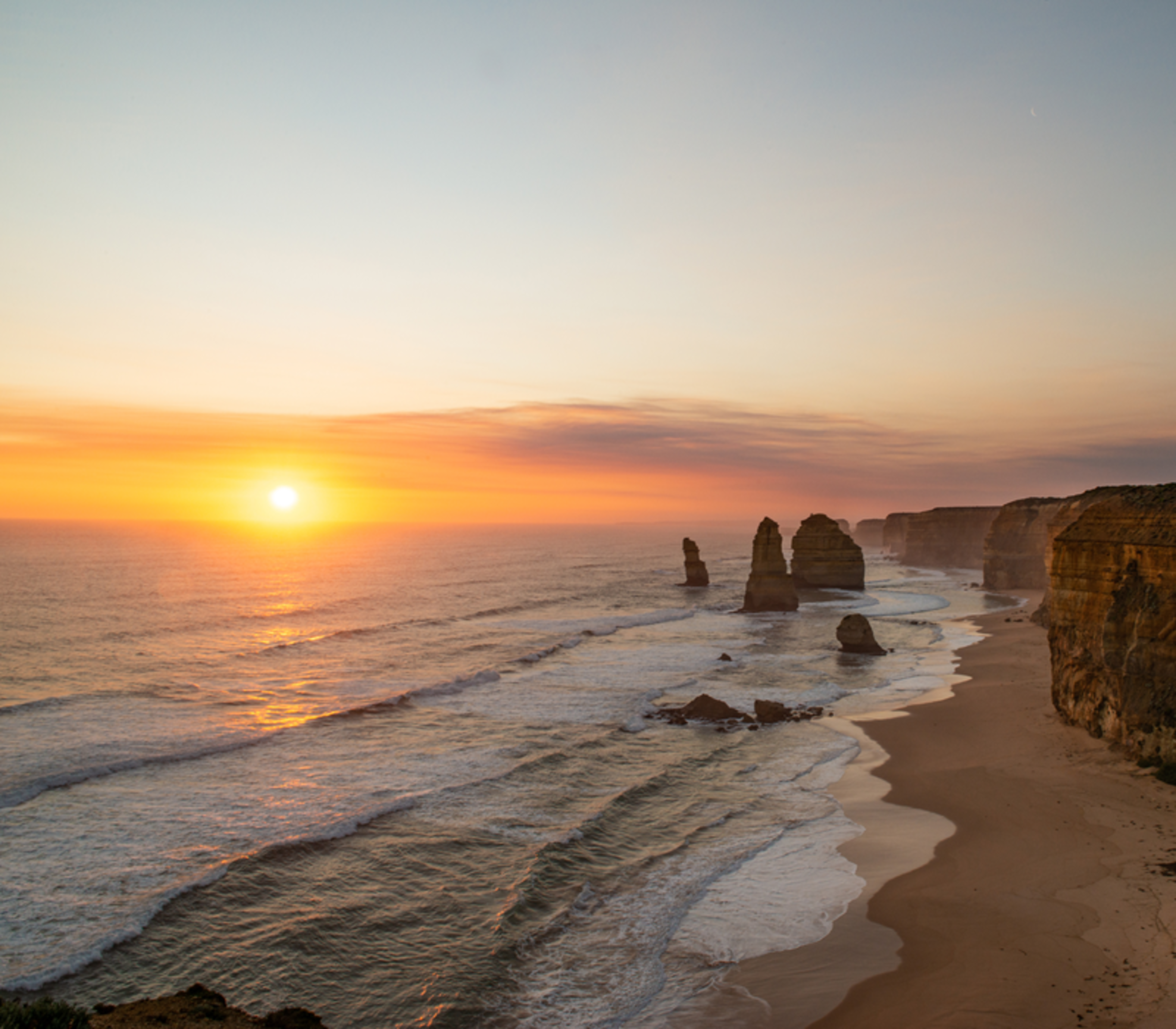 Panoramic sunset over the Twelve Apostles stacks and beach along the Great Ocean Road, Victoria.