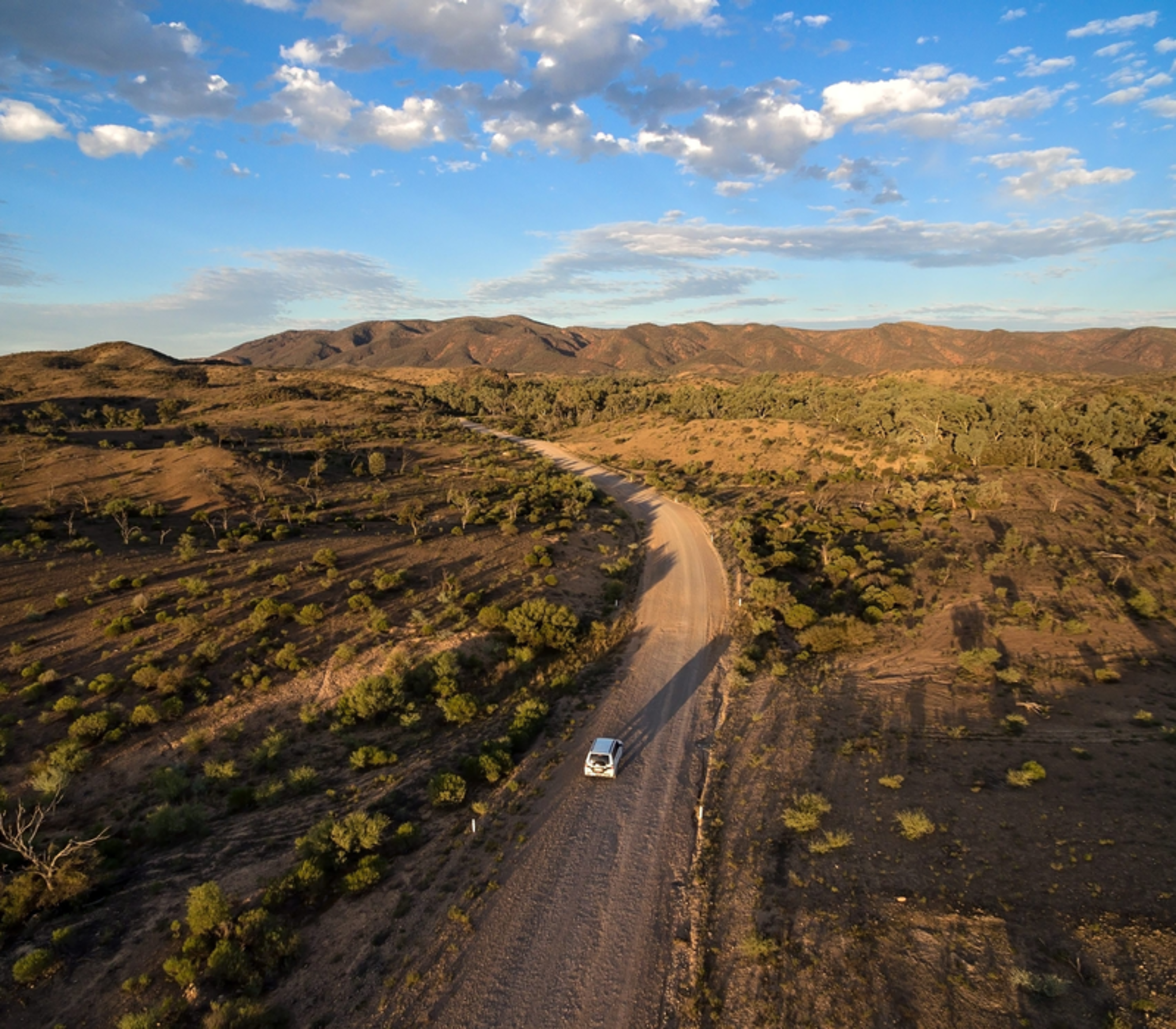 High angle view of a white car driving on a dirt road through the ancient hills of the Gammon Ranges in South Australia.