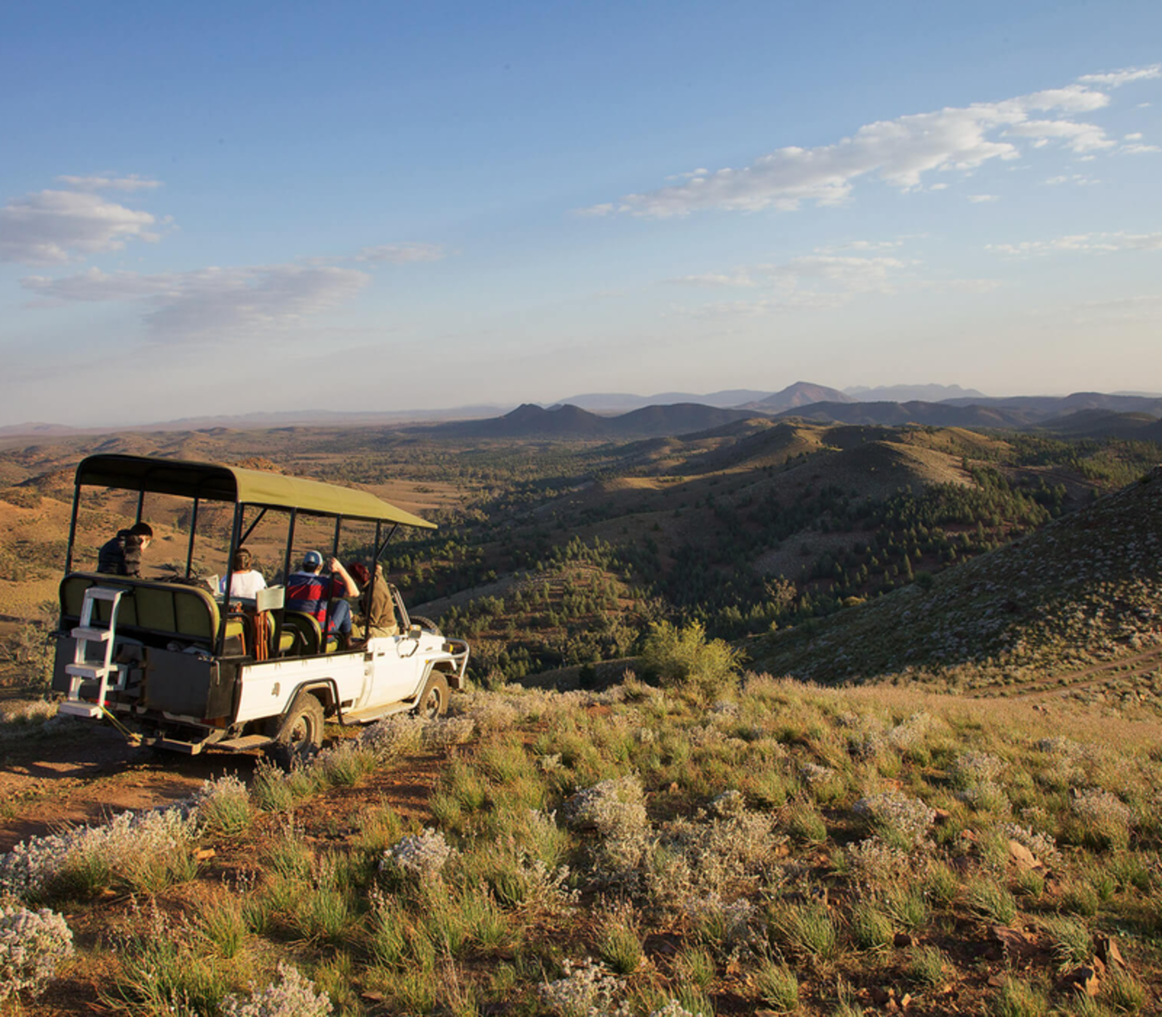 A white open-air safari vehicle parked on a ridge overlooking a vast valley in the Australian outback.