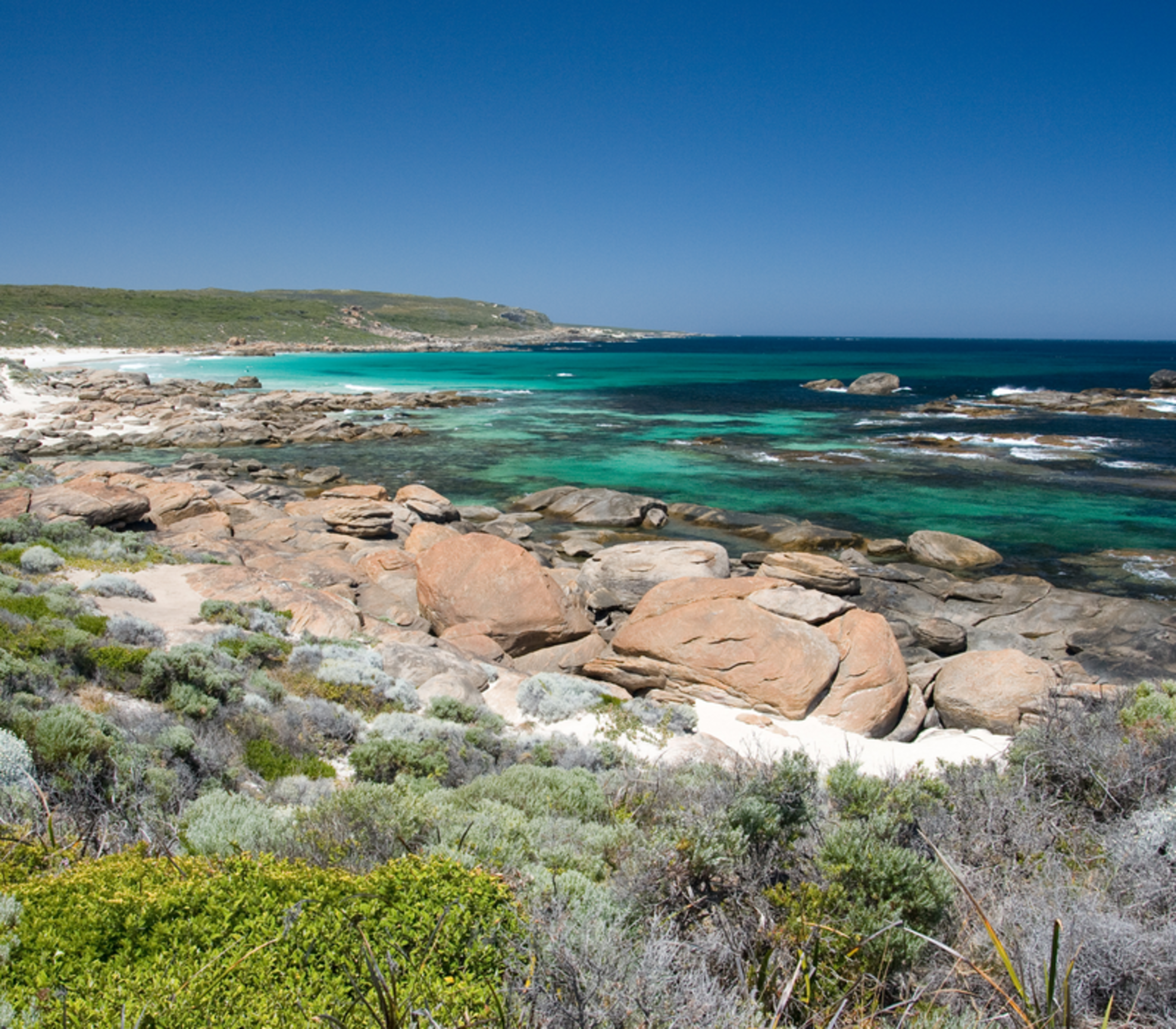 Scenic view of large orange-tinted rocks on a white sand beach with clear green and blue ocean water.