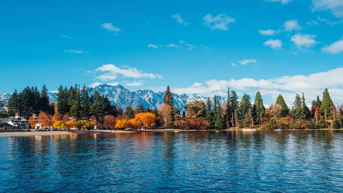 Autumn trees and snow-capped mountains reflected in lake water at Queenstown. Main Image