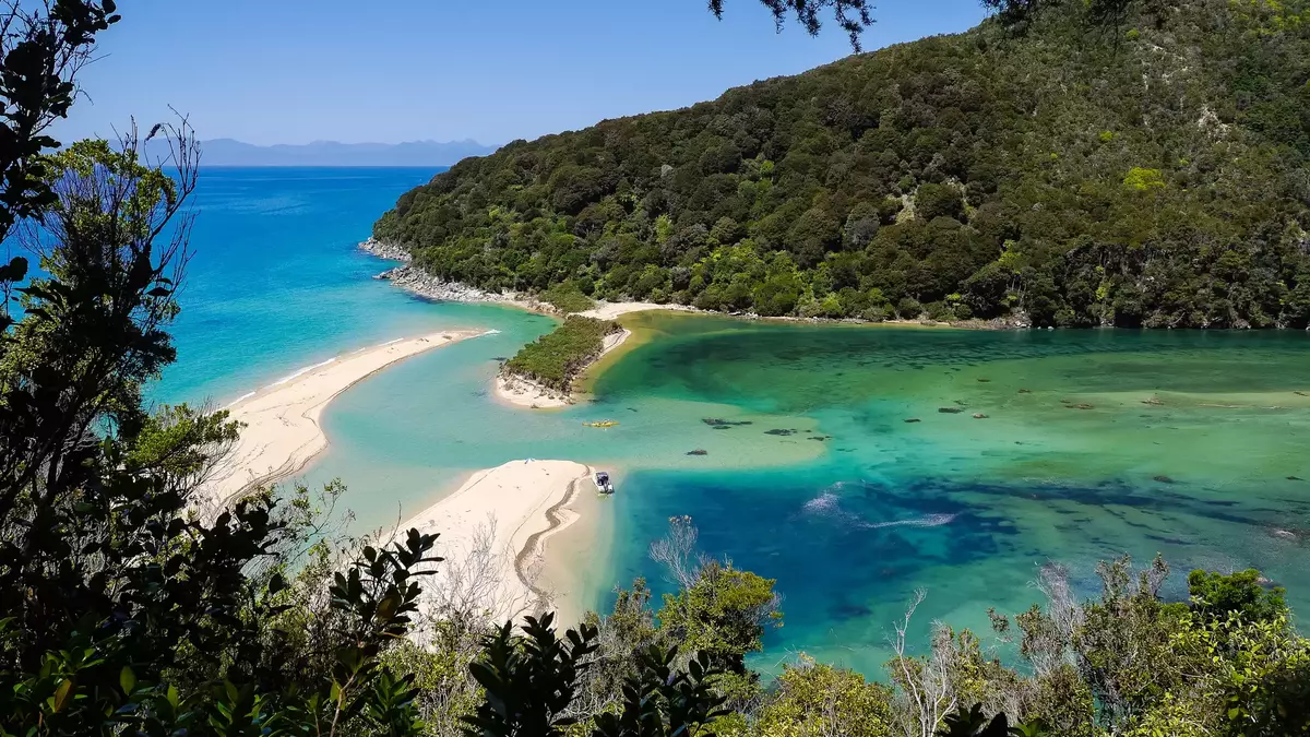 A white sandbar separates a deep blue ocean from a turquoise tidal lagoon and forest. Main Image