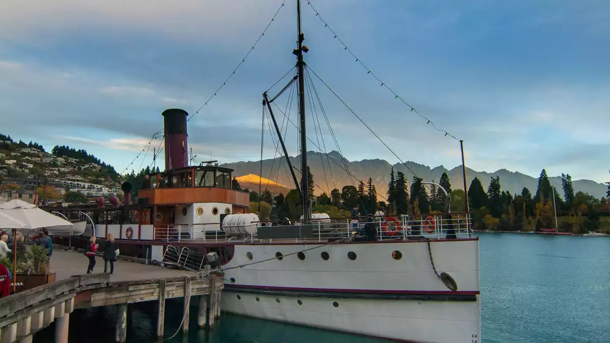 Steamship docked at a pier with mountains and water in the background during sunset. Main Image